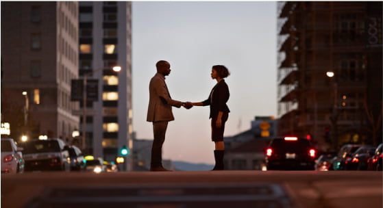 都会の道の真ん中で握手を交わす２人の画像